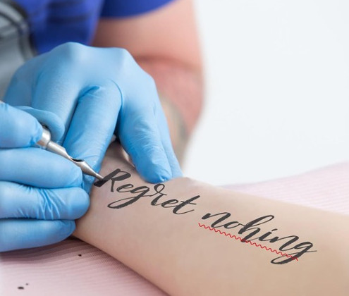 Text "Regret nothing" is tattooed on an arm, but with a typo: nohing instead of nothing