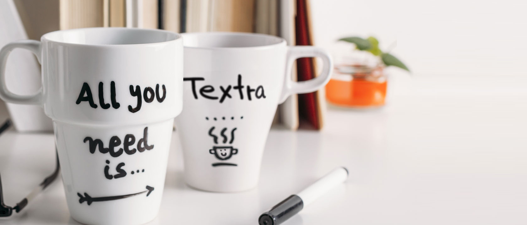 Zwei Kaffeetassen auf einem Schreibtisch mit der Aufschrift: „All you need is Textra“.